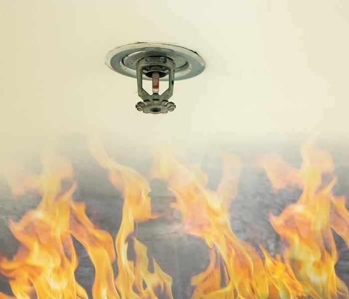 Fire sprinkler head on white ceiling in a building with flames below. 